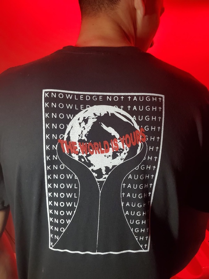 Genesis — the first KNT tee, worn, printed with a globe graphic and the words The World Is Yours